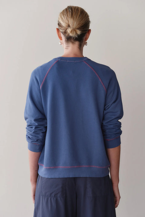 Close-up of raspberry contrast stitch detail on DONNI lapis blue eco terry sweatshirt – organic cotton texture